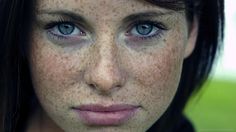 a woman with freckles on her face and blue eyes looks at the camera