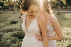 two beautiful women standing next to each other in front of some trees and grass with the sun shining on them