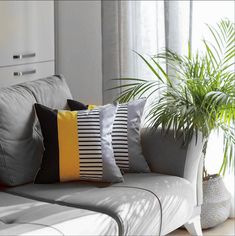 a yellow couch with black and white pillows in front of a potted palm tree