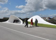 several people walking on the side of a road next to a large white structure that is shaped like a cone