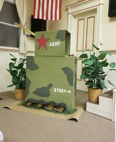 an army tank made out of cardboard sitting on the floor next to potted plants