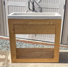 a white sink sitting on top of a wooden stand in front of a building next to a fence