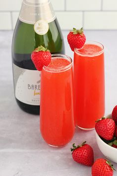 two glasses filled with liquid and strawberries next to a bottle