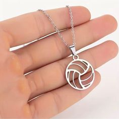 a hand holding a silver necklace with a volleyball ball on the front and back of it