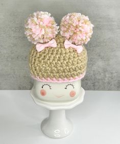 a crocheted hat with two pom poms on top, sitting on a mannequin head