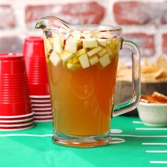 a pitcher filled with apples sitting on top of a table next to cups and plates