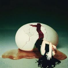 a woman is laying on the ground next to an egg that has been cracked in half