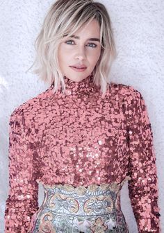 a woman with blonde hair wearing a red sequin top and silver skirt standing in front of a white wall