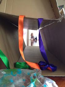 an open cardboard box with ribbon on the floor and a child sitting in the background