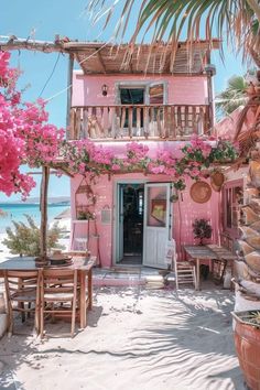 a pink house on the beach with flowers hanging from it's balcony and table