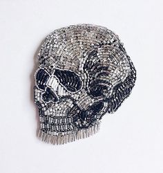 a silver and black beaded skull brooch sitting on top of a white surface