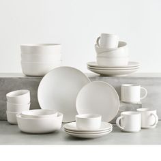 white dishes and cups are stacked up on a countertop, with one empty plate in the middle