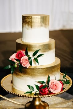 a three tiered wedding cake with pink flowers on the top and gold trimmings