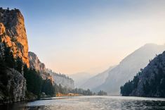 the sun is shining on some mountains and trees in the distance, along side a body of water