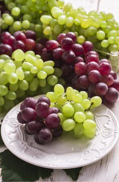 grapes are arranged on a white plate next to some green and red grapes in a glass vase