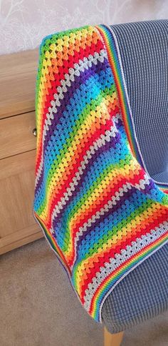 a colorful crocheted blanket sitting on top of a blue couch next to a wooden dresser