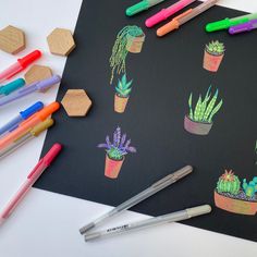 some markers and pens are sitting on a table next to a blackboard with various succulents