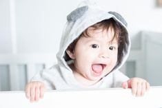 a baby wearing a hoodie and sticking his tongue out from behind a crib