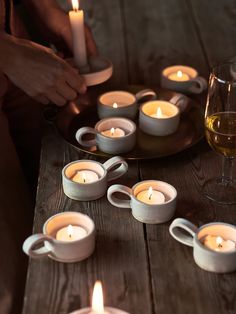 several tea lights on a wooden table next to wine glasses and a plate with candles