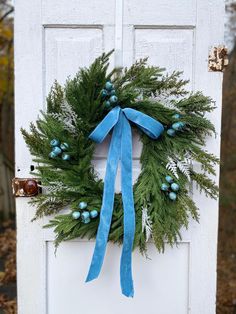 a wreath is hanging on the front door with blue ribbon and ornaments around it's edges