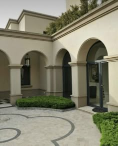 an outdoor courtyard with circular hedges and stone walkways, surrounded by white stucco walls