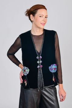 a woman wearing black leather pants and a black vest with flowers on the back, standing in front of a gray background