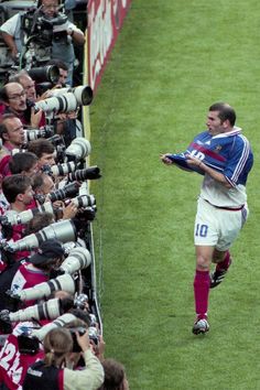 a soccer player is running on the field with his arms in the air and cameras around him