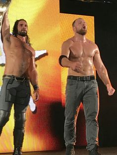 two shirtless men standing on stage with one holding a trophy in the other's hand