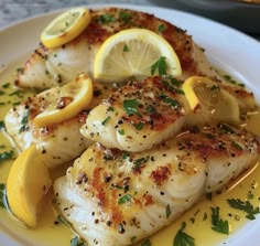 a white plate topped with fish covered in lemon slices and garnished with parsley