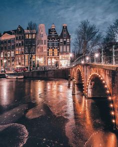 a bridge that is over some water with lights on it and buildings in the background