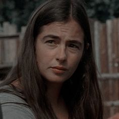 a woman with long hair standing in front of a fence and looking at the camera