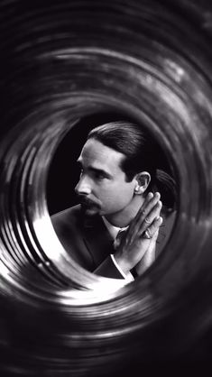 a man in a suit is looking out from inside a metal tube with his hands clasped