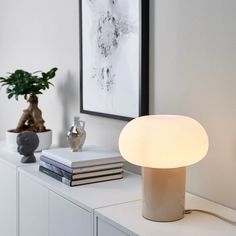 a white lamp sitting on top of a table next to a potted plant and books