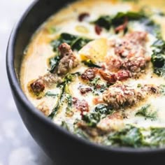 a close up of a bowl of soup with meat and spinach in it on a table