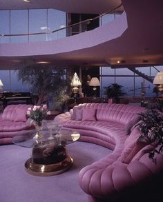 a living room filled with purple couches next to a tall glass window overlooking the ocean