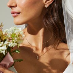 a woman in a wedding dress holding a bouquet of flowers and wearing a diamond necklace