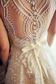 the back of a woman's wedding dress with beading and pearls on it