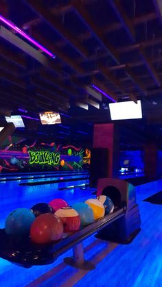 a bowling alley with several balls on the side and neon lights in the back ground