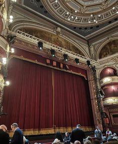 an auditorium with red curtains and people sitting in the seats looking up at the stage