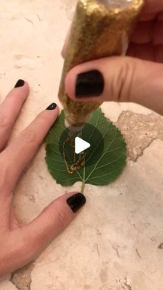 a woman with black and gold nail polish holding a green leaf