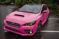 a pink subarunt parked in a parking lot next to some bushes and trees