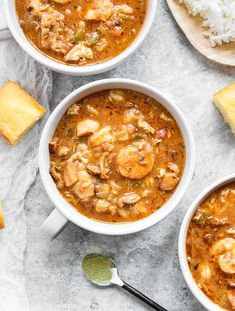 three bowls of shrimp and rice soup with spoons on the table next to it