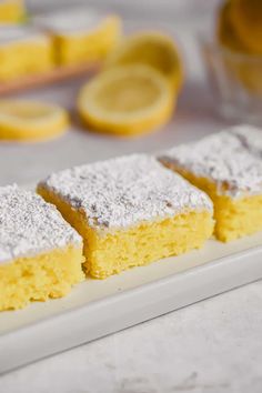 three slices of lemon cake on a white plate with powdered sugar and lemons in the background