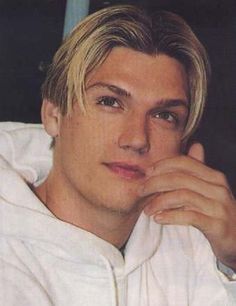 a young man with blonde hair wearing a white hoodie and looking at the camera