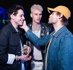 three young men standing next to each other at a party, one holding a drink in his hand