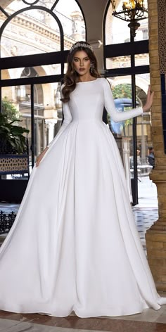 a woman in a white wedding dress standing next to a window with her hands on her hips