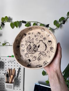 a person holding a bowl with drawings on it in front of a wall mounted plant