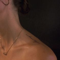 the back of a woman's neck with a cross tattoo on her left shoulder