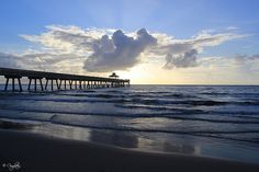 the sun is setting over the ocean with a pier stretching into the distance from the beach