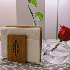 a vase with a red rose in it next to a card holder on a table